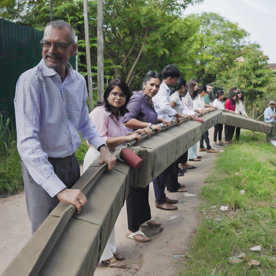 A line of community volunteers guiding a long canvas boom along a canal-bank railing during a MAS Foundation for Change field engagement