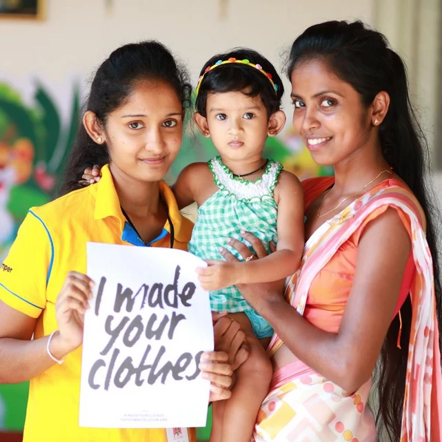Two MAS team members and a child holding an “I made your clothes” sign at a MAS Bodyline 1 Local Connect event