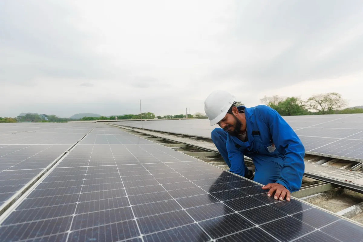 A technician in blue overalls and a white hard hat installing rooftop solar panels at a MAS facility