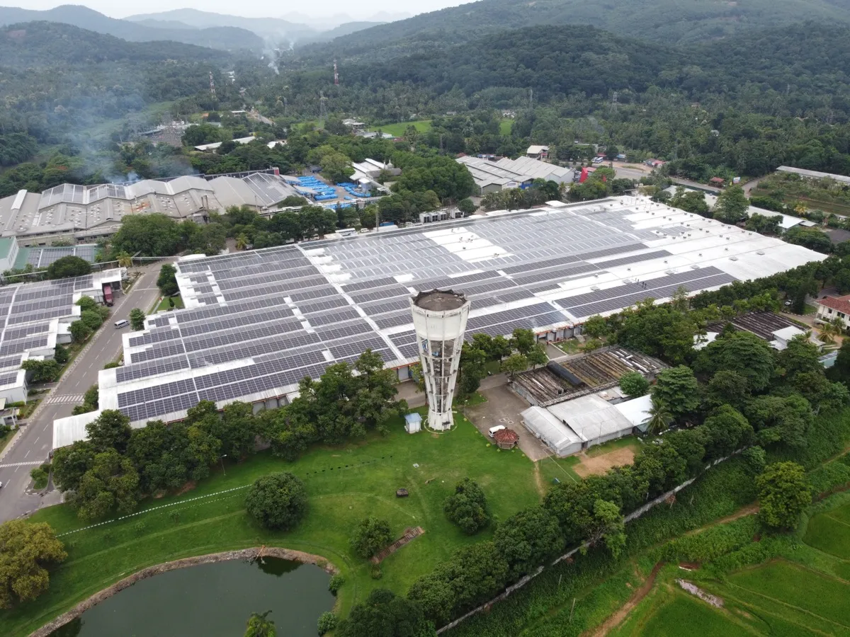 Aerial view of MAS Fabric Park — solar-roofed industrial buildings beside a water tower, surrounded by greenery
